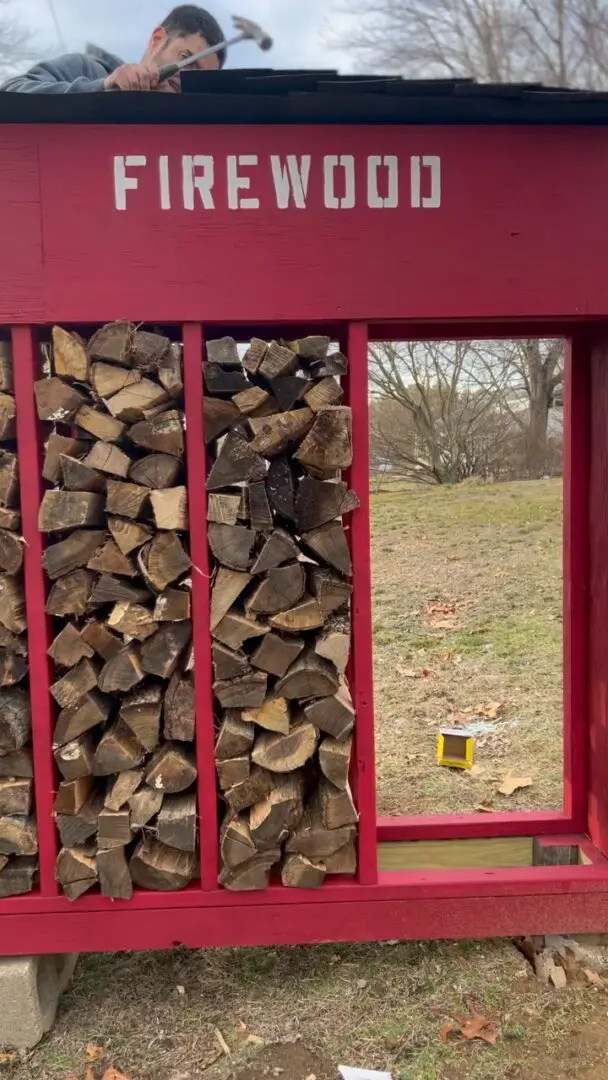 A red wooden fence with logs stacked up on top of it.